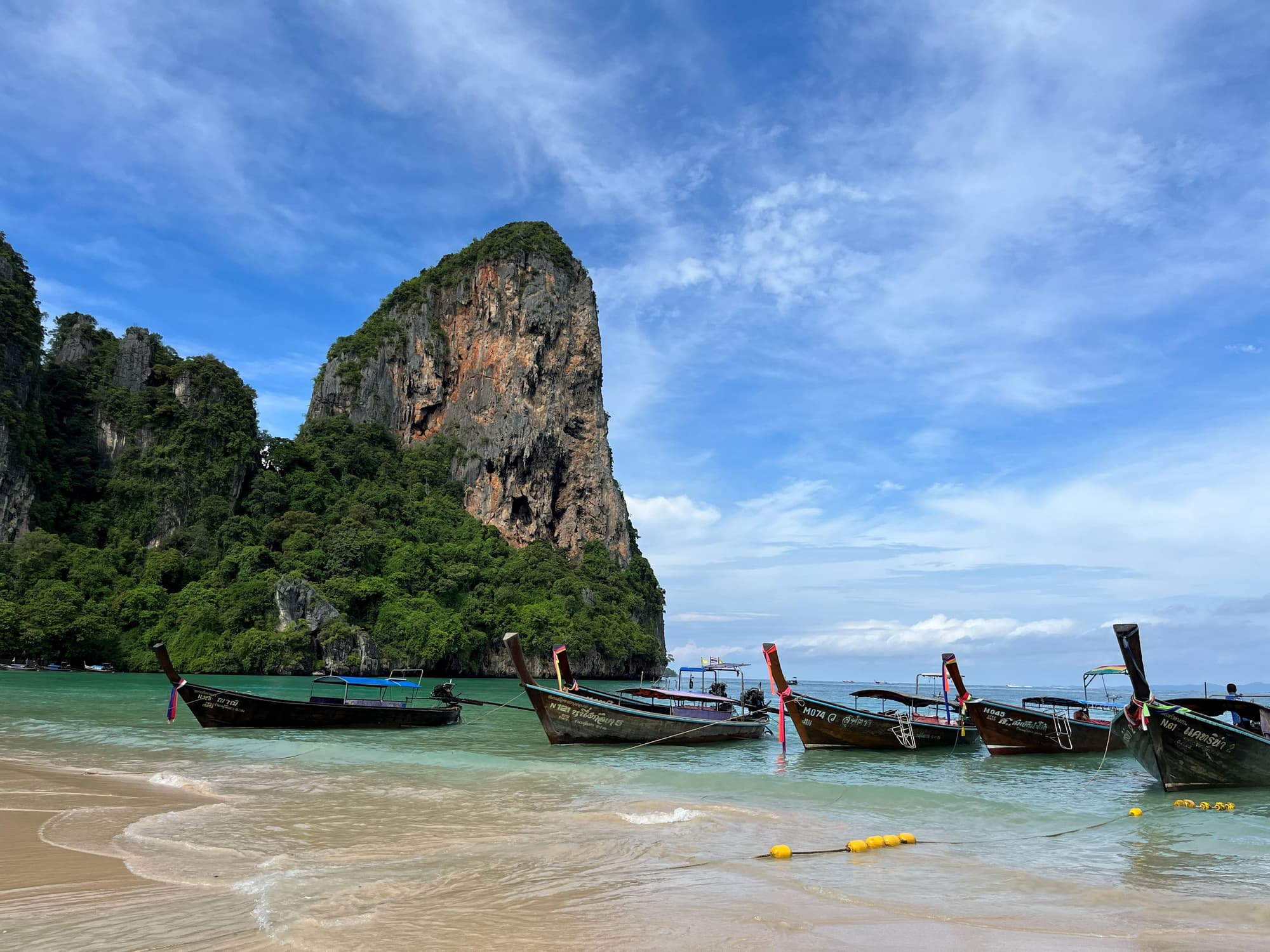 Longtail boats on the beach near a limestone rock formation
